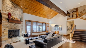 A spacious living room with a stone fireplace, a large black leather sofa, and a wooden staircase. - Luxury Home DV Mid Mountain, Skier Shuttle, Game/Theater Rooms, Hot tub (Deer Valley)
