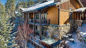 A lodge with a stone chimney, a hot tub, and a deck overlooking a snowy landscape. - Luxury Home DV Mid Mountain, Skier Shuttle, Game/Theater Rooms, Hot tub (Deer Valley)