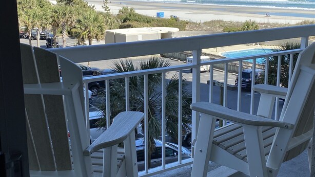 A balcony with white chairs overlooking a beach and ocean.