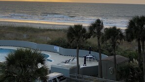 A beach view with a pool area, including lounge chairs and umbrellas.