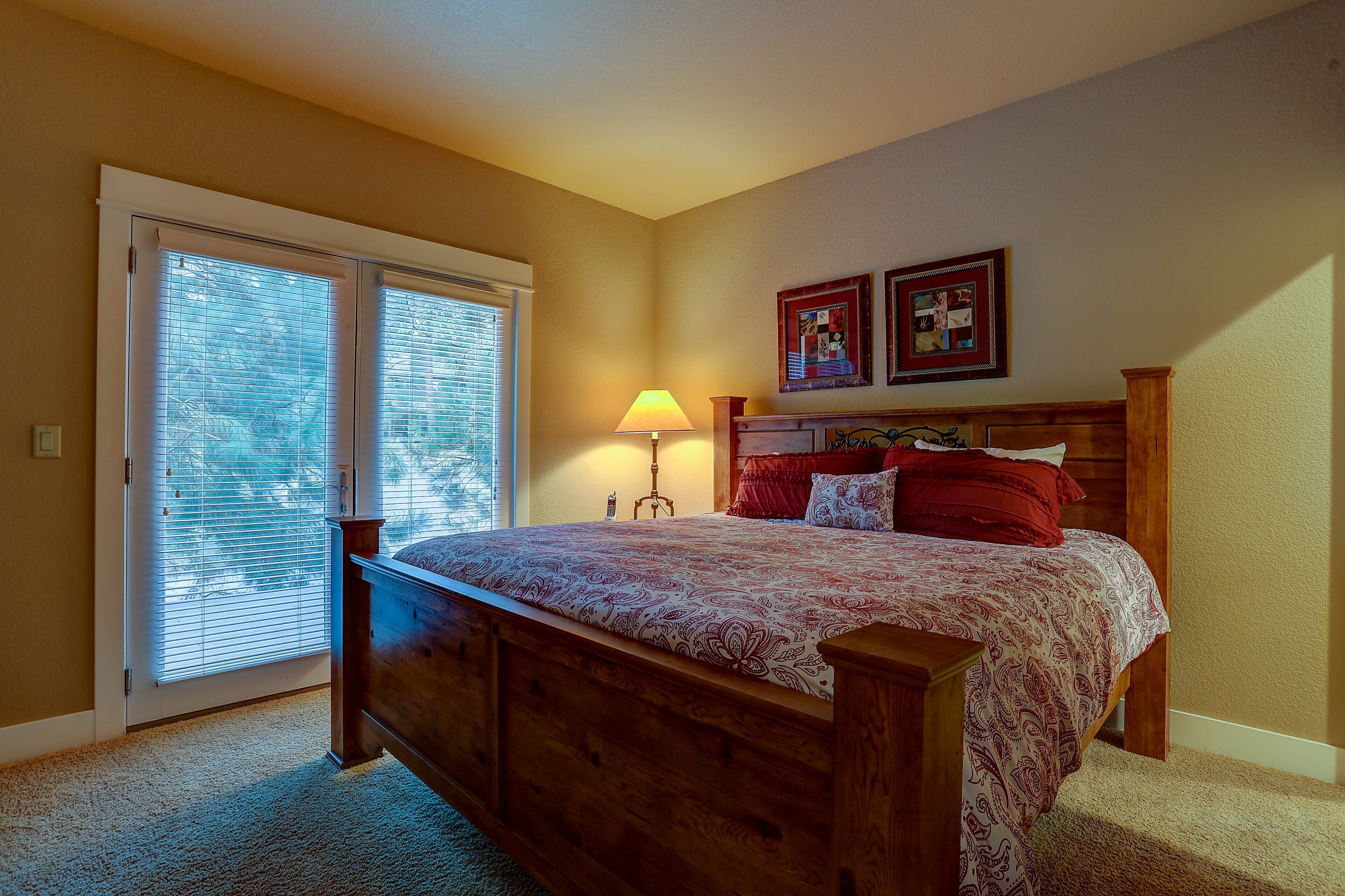 A bedroom with a wooden bed, a nightstand, a lamp, and a window with blinds.