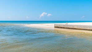 A beach with clear blue water, a sandy shore, and a concrete barrier. - Pet Friendly | Community Pool | Beach Access (Gulf Shores)