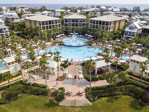 Een luchtendichtbeeld van een resort met een centraal zwembad, omringd door palmbomen en liggedeeltes.