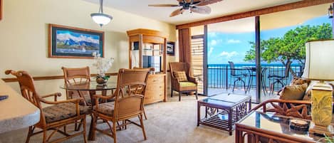 A room with wicker furniture, a glass table, and a view of the ocean.