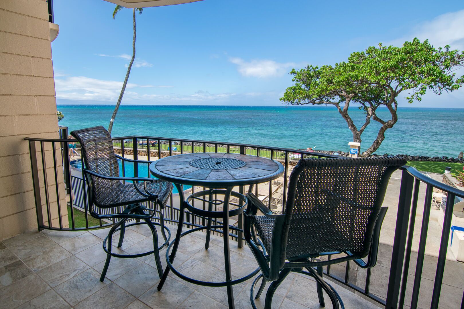 A balcony with a round table and four chairs, overlooking a pool and the ocean.