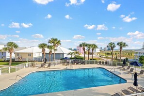 A swimming pool with lounge chairs and umbrellas, surrounded by palm trees and buildings. - 1BR Fort Morgan Condo | Gulf & Sunset Views (GULF SHORES)
