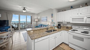 A kitchen with white cabinets, a granite countertop, a stove, and a view of the ocean.
