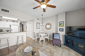 A modern kitchen with white cabinets, a dining area with a round table and chairs, a ceiling fan, and a TV cabinet. - 1BR Fort Morgan Condo | Gulf & Sunset Views (GULF SHORES)