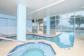 Une piscine intérieure avec des parois en verre transparent, un jacuzzi et une vue sur les palmiers à l’extérieur.