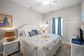 A bedroom with a bed, nightstand, lamp, television, and artwork on the walls. - 1BR Fort Morgan Condo | Gulf & Sunset Views (GULF SHORES)