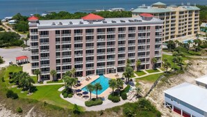 A multi-story hotel with a swimming pool, surrounded by greenery and a view of the ocean.