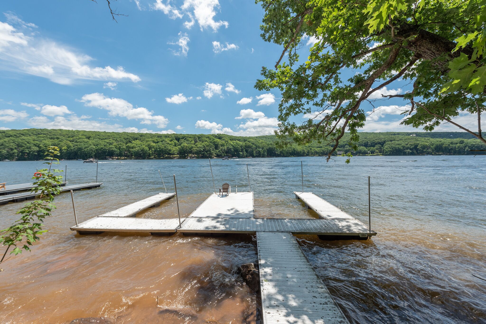 A dock extending into a lake with a clear sky and a forested hill in the background.