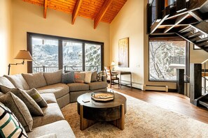 Un salón acogedor con un sofá modular, una mesa de centro redonda y vistas a montañas nevadas a través de amplios ventanales.