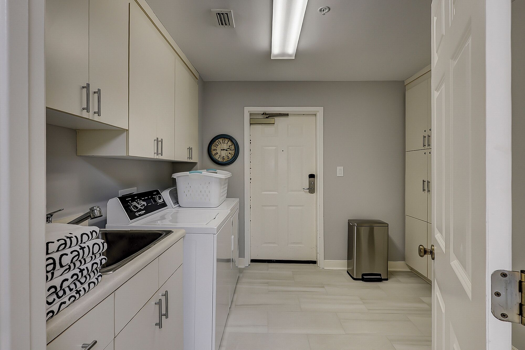 A laundry room with a washing machine, dryer, and a trash can.
