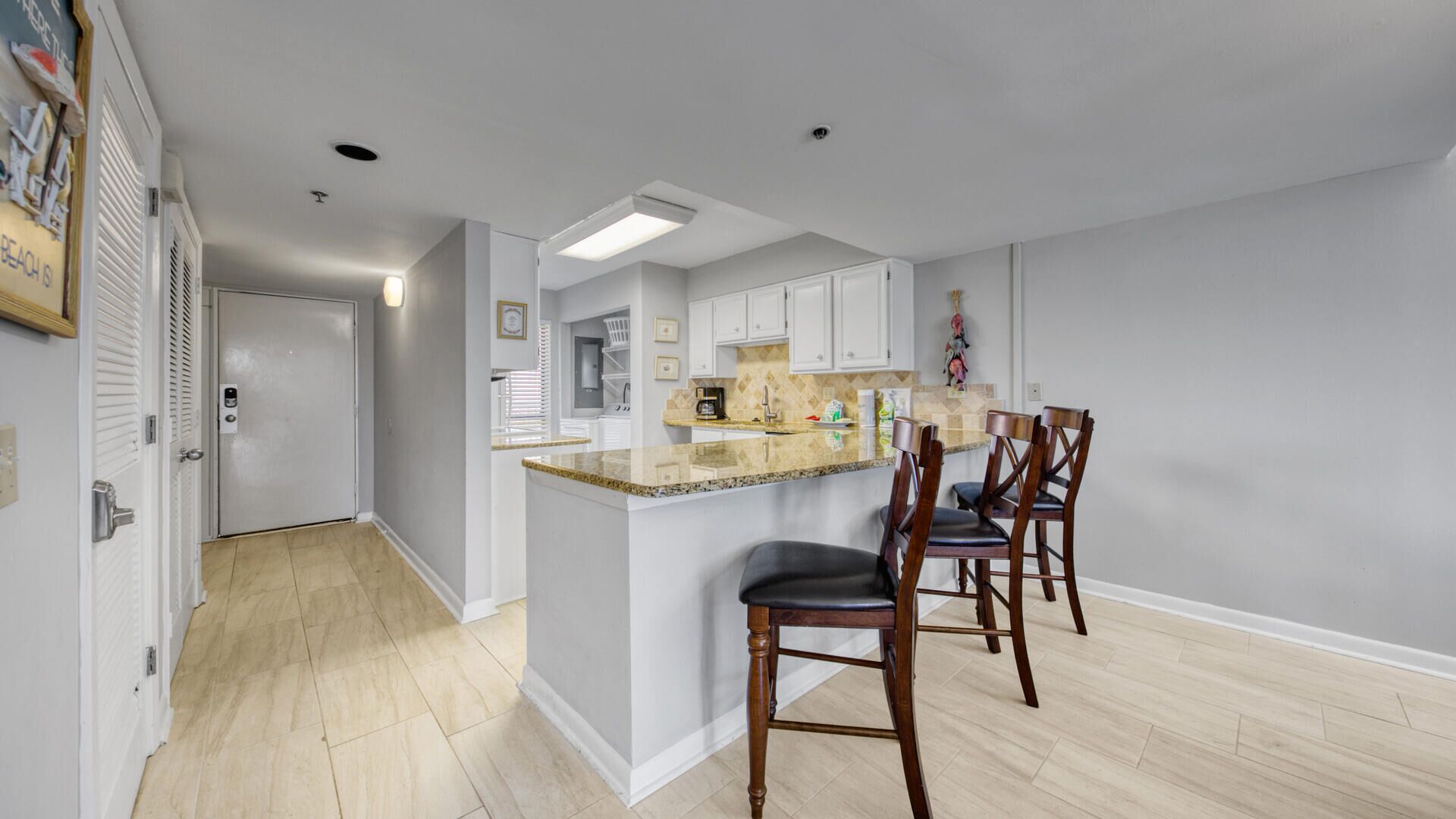 A modern kitchen with a central island, wooden chairs, and white cabinets.