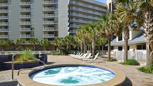 A hot tub surrounded by lounge chairs and palm trees, with a building in the background. - Gulf View! Coastal Chic! Mainsail 288! (Miramar Beach)