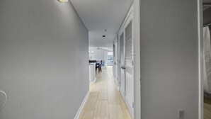 A narrow hallway with light-colored walls and wooden flooring, leading to a dining area with a table and chairs. - Gulf View! Coastal Chic! Mainsail 288! (Miramar Beach)