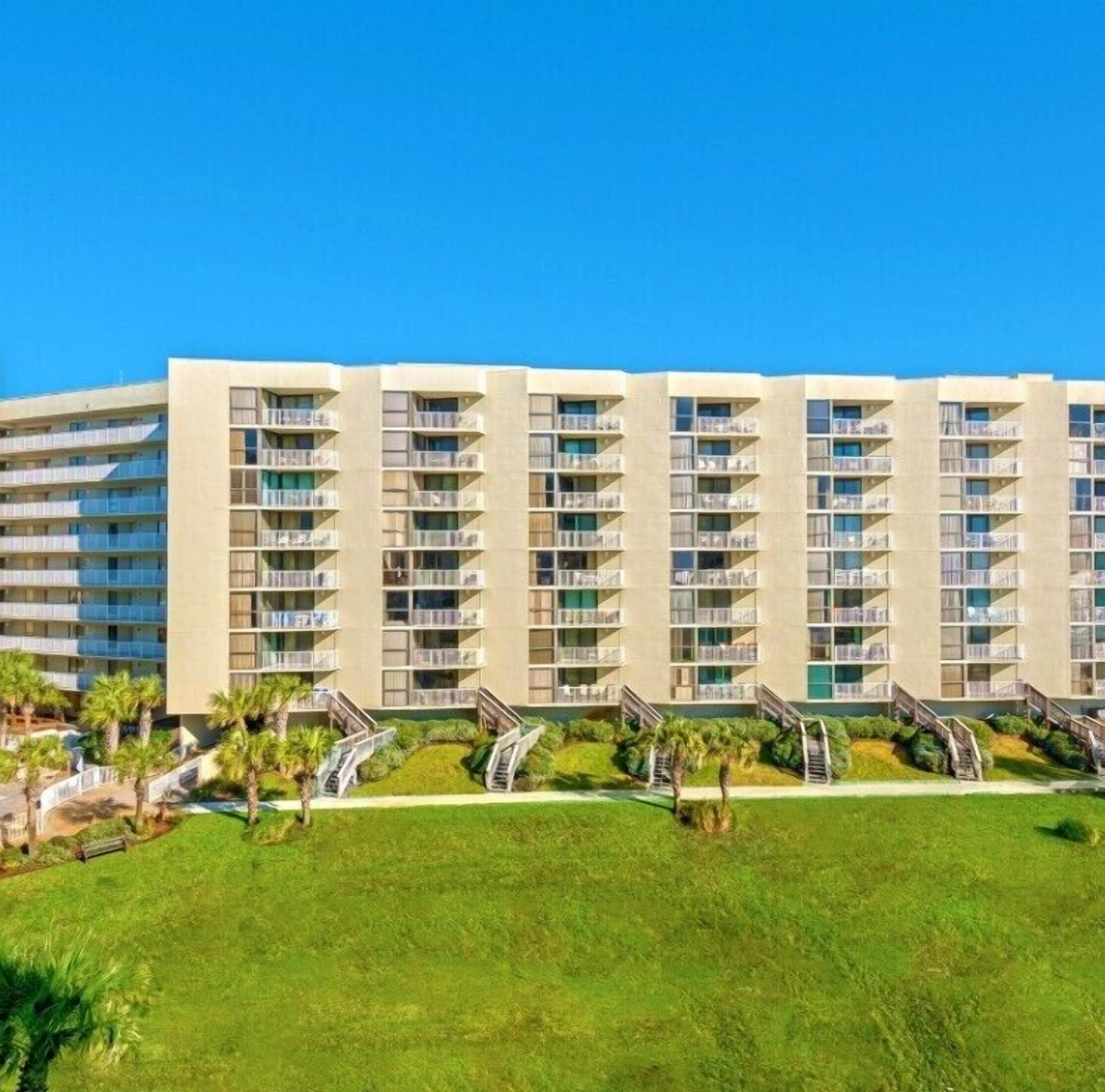 A multi-story hotel with balconies, a central courtyard, and palm trees.