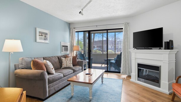 A living room with a sofa, coffee table, fireplace, TV, and large windows.