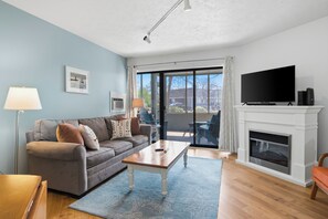 Una sala de estar con sofá, mesa de centro, chimenea, televisor y ventanas amplias.