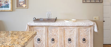 A kitchen with a granite countertop, a wooden cabinet with intricate carvings, and a white tablecloth-covered island.