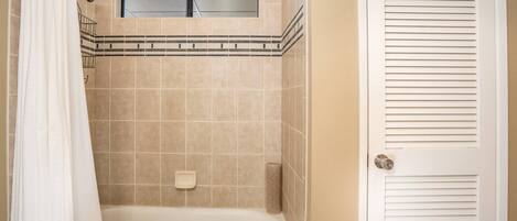 A bathroom with a bathtub, a shower curtain, a toilet paper holder, and a door with a louvered panel.