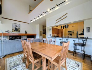 Un coin repas avec une table et des chaises en bois, une cheminée, un canapé et, au fond, une cuisine.