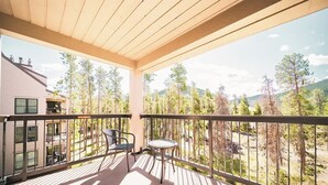 Ein Balkon mit Blick auf Bäume und Berge, ein Stuhl und ein Tisch.