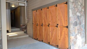 Eine Holztür zur Garage mit schwarzen Scharnieren, eine Steinmauer und ein Betonweg, der zu einer Treppe führt.