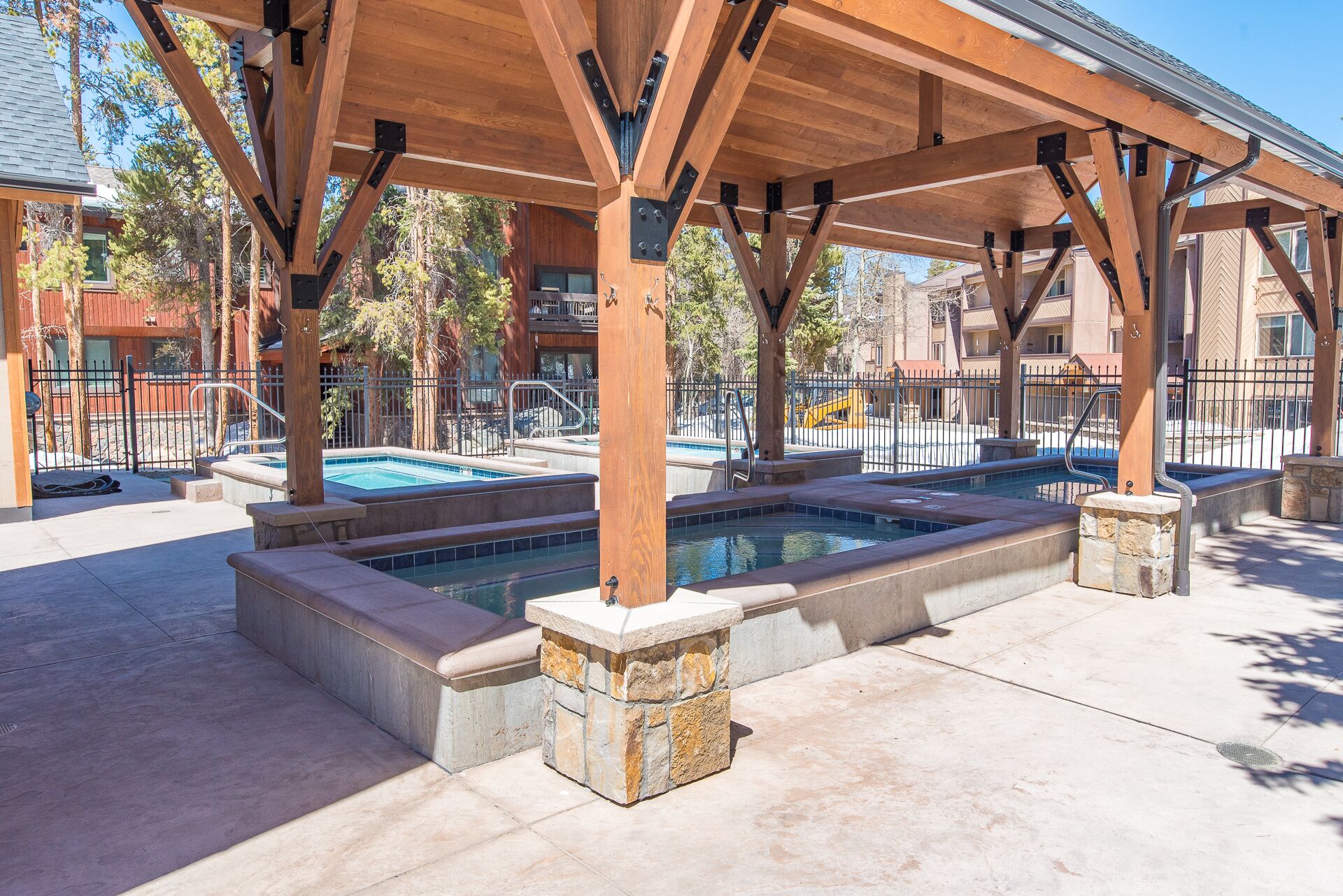 A covered outdoor pool area with multiple hot tubs, stone steps, and a wooden pergola structure.