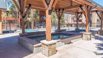 A covered outdoor pool area with multiple hot tubs, stone steps, and a wooden pergola structure.