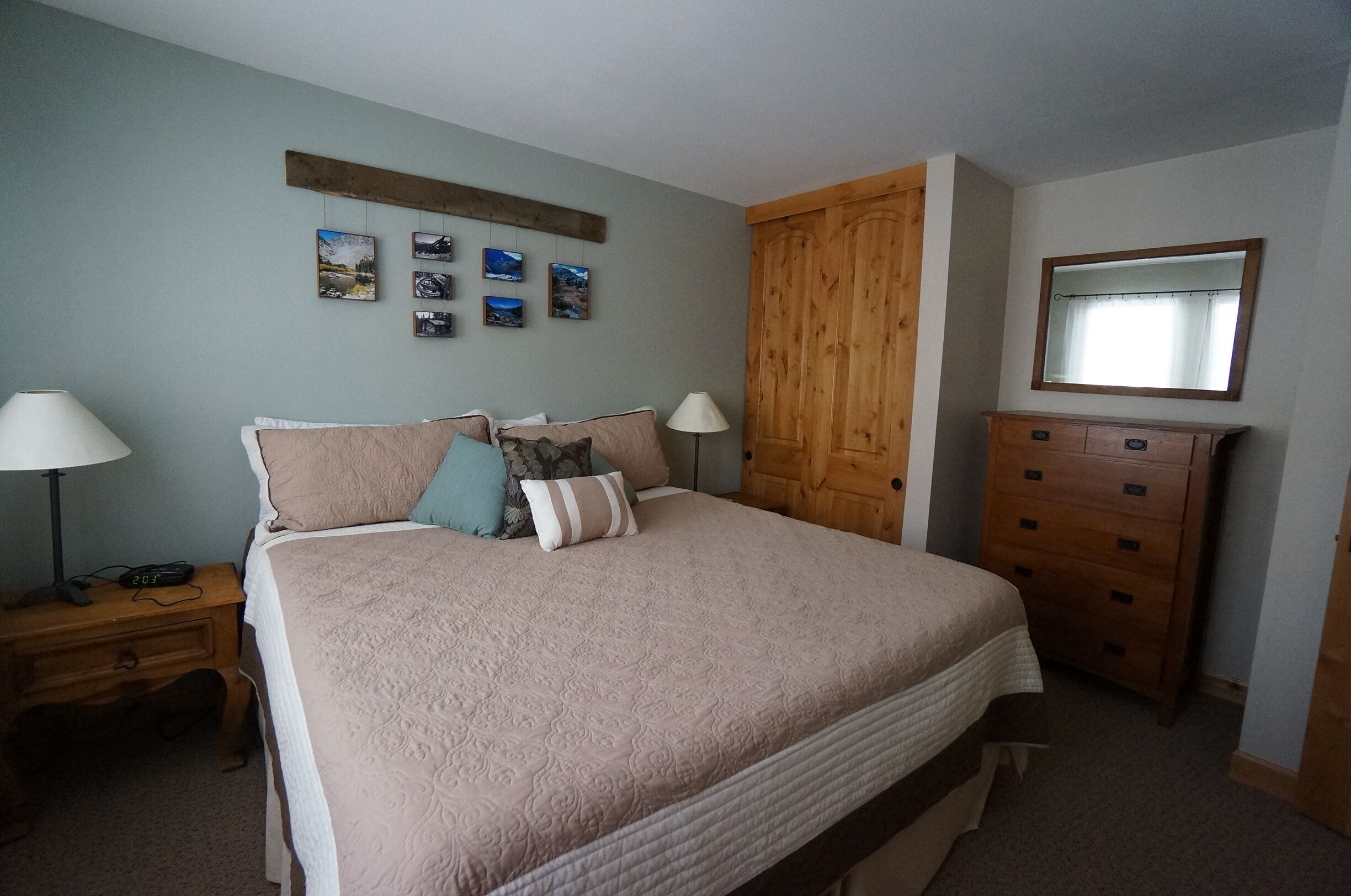 A bedroom with a large bed, wooden wardrobe, and a nightstand with a lamp.