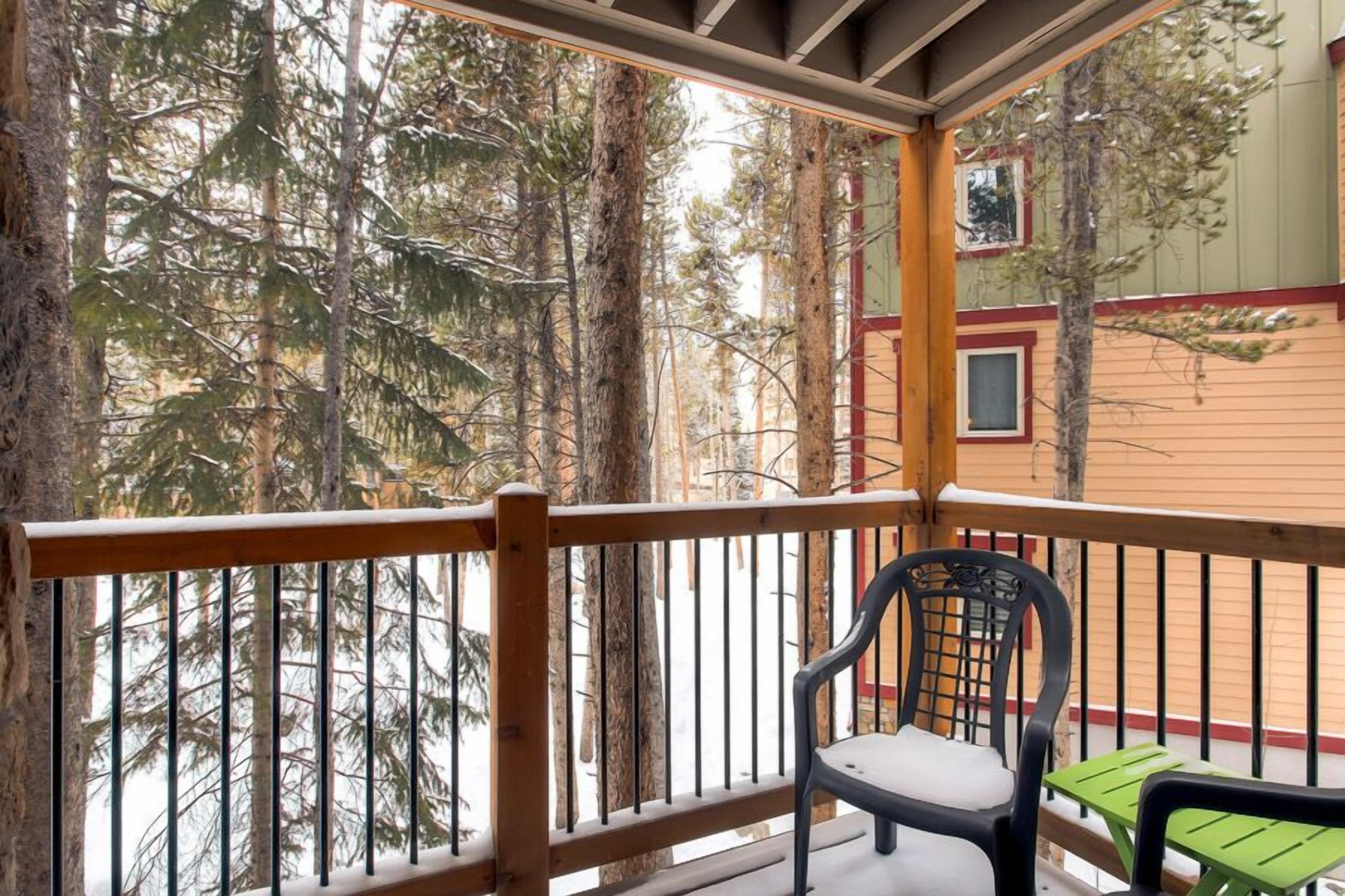 Un balcon en bois avec une chaise et une petite table, donnant sur une zone boisée.