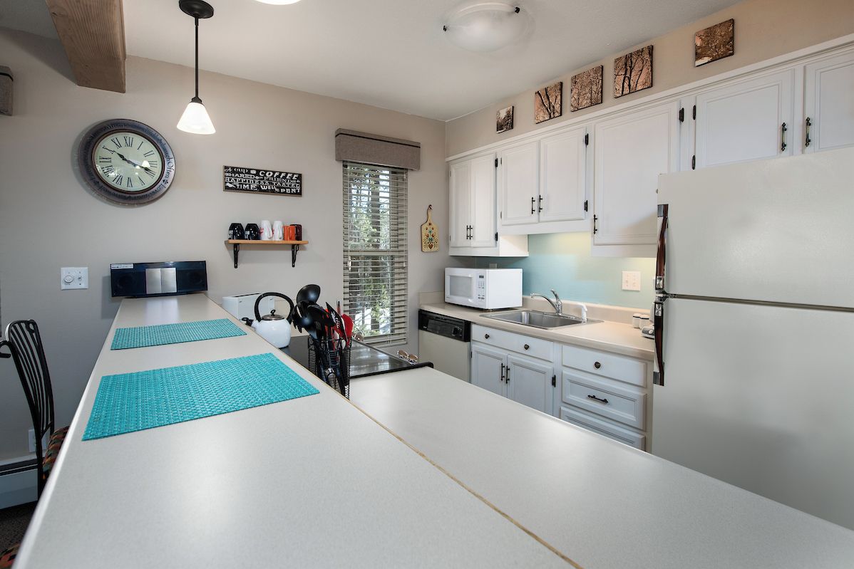 A modern kitchen with white cabinets, a microwave, a refrigerator, and a clock on the wall.