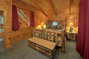A cozy log cabin bedroom with a wooden bed, a bench, two lamps, and a window with curtains.