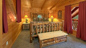 Un dormitorio tipo cabaña de troncos con una cama de madera, dos lámparas de noche, un banco de madera y un ventanal con cortinas.