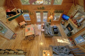 A spacious cabin with a wooden interior, a fireplace, a television, and a dining area.