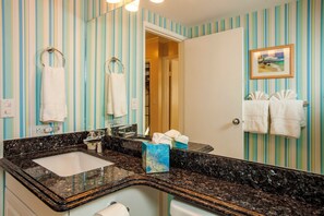 A bathroom with striped wallpaper, a marble sink, and towels hanging on hooks.