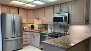 A modern kitchen with light wood cabinets, stainless steel appliances, a granite countertop, and a central island. - Waiohuli Beach Hale #D-122 Oceanfront Complex, Great Rates, Ground Floor Unit (Kihei)