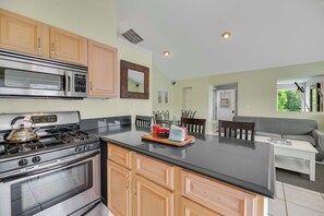 A kitchen with wooden cabinets, a stainless steel stove, and a microwave. There is a dining area with a table and chairs.