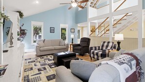 Ein geräumiges Wohnzimmer mit hoher Decke, einem Deckenventilator, einer Treppe und Blick ins Freie.