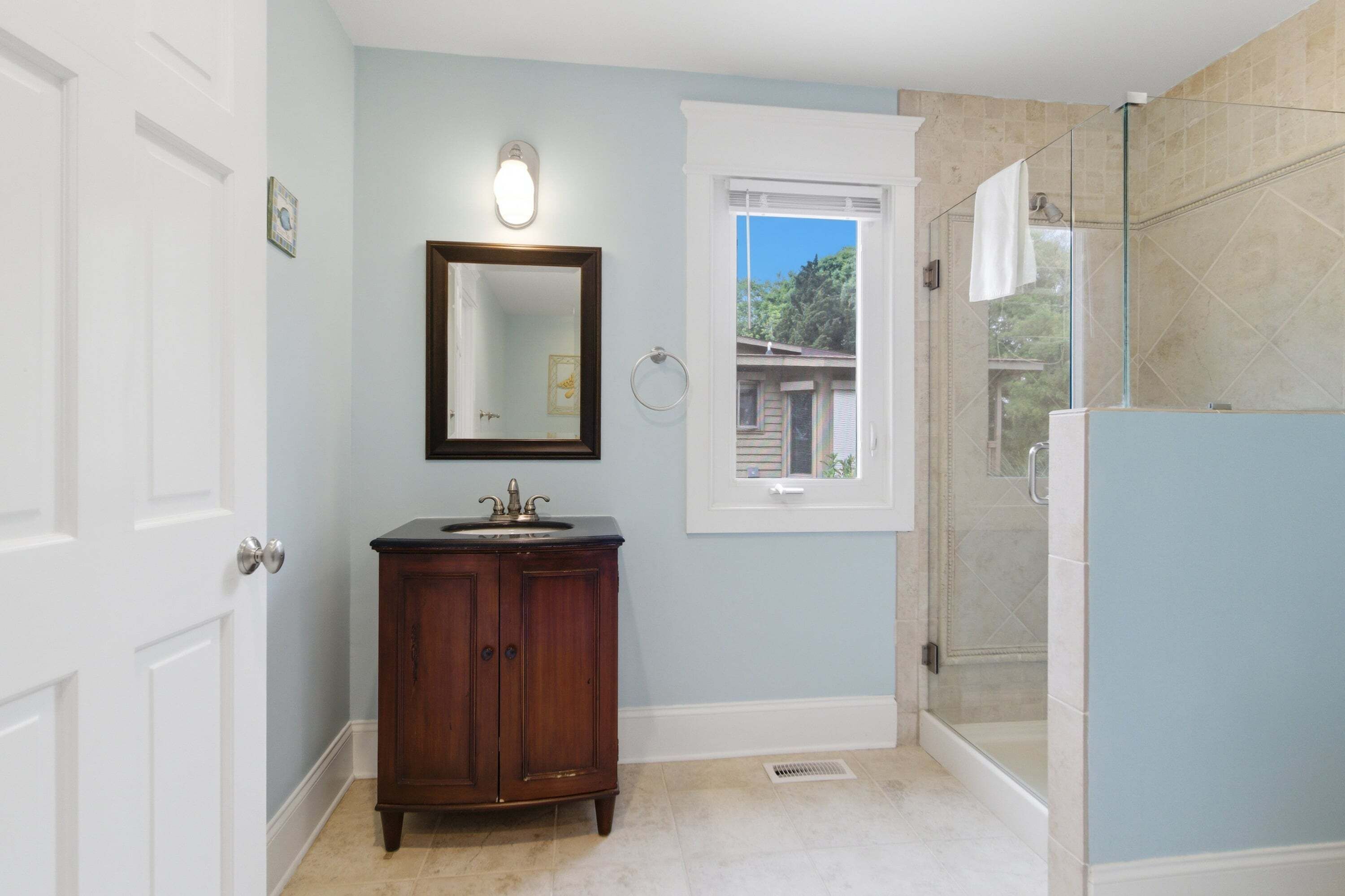 A bathroom with a vanity, a mirror, a window, and a shower area.