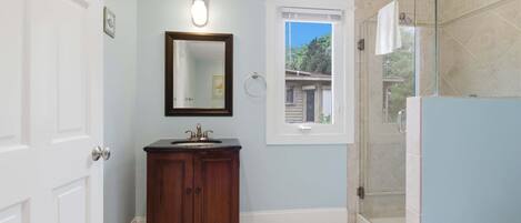A bathroom with a vanity, a mirror, a window, and a shower area.