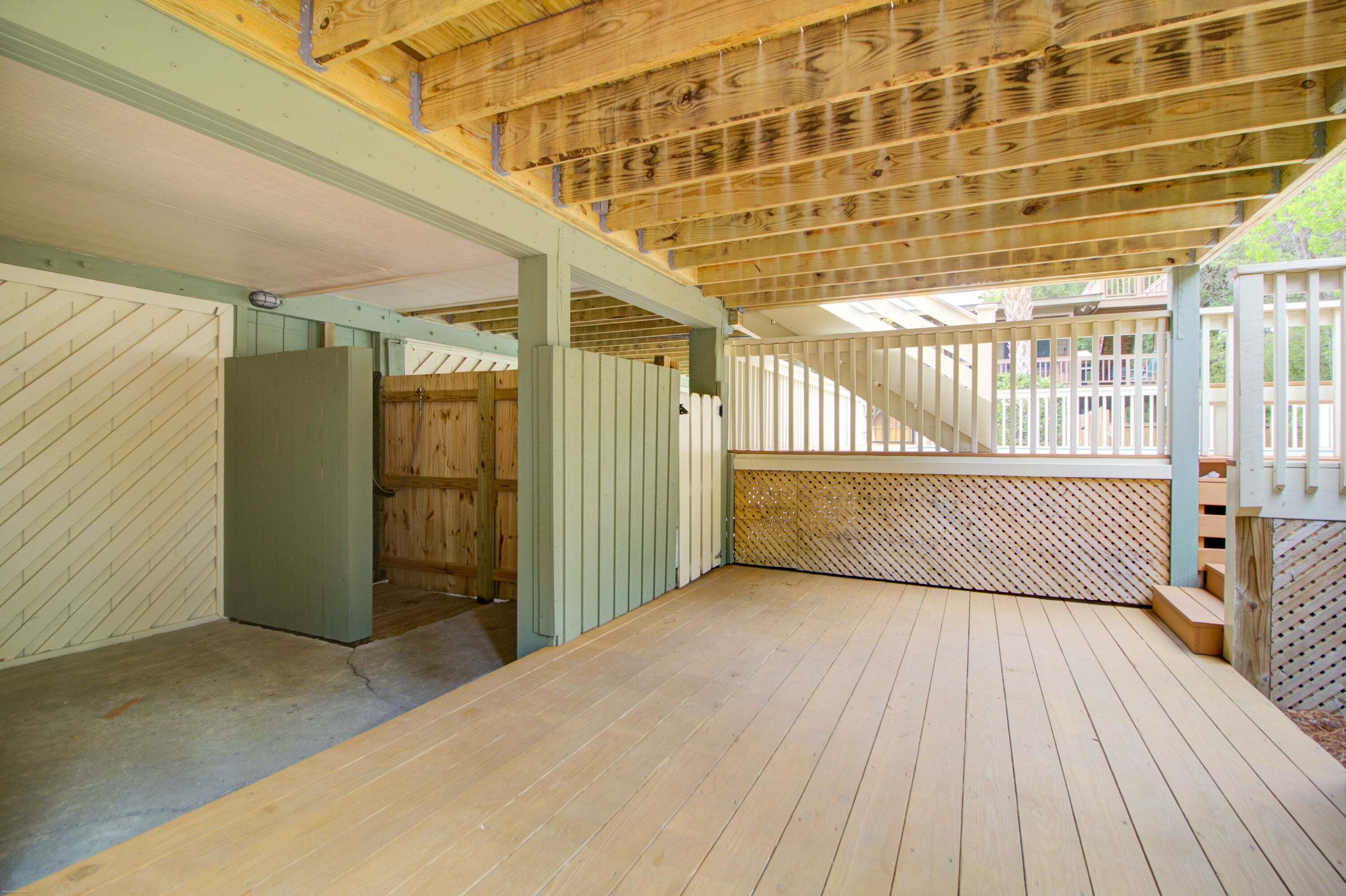 Una terraza de madera abierta con vista a una casa al fondo.