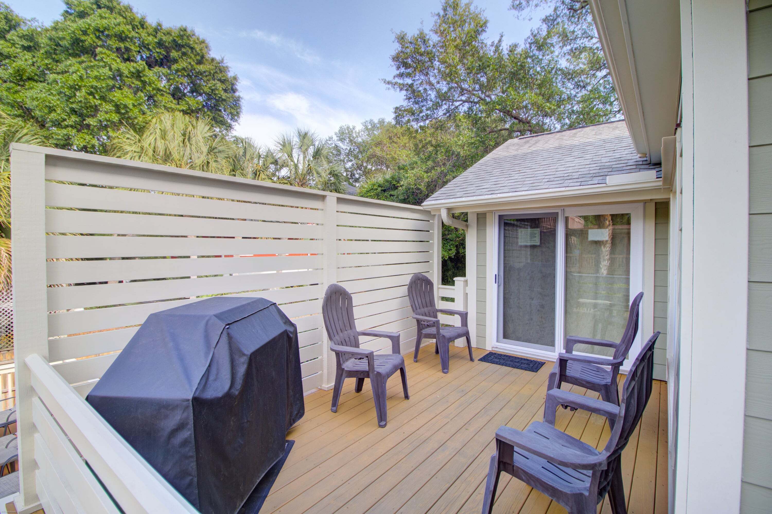 Une terrasse avec des chaises et un barbecue, une clôture blanche et une porte-fenêtre coulissante.
