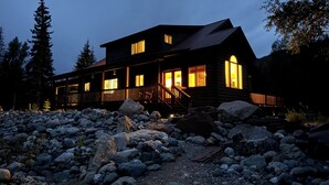 Une cabane en rondins dotée d’une terrasse en bois, de grandes fenêtres et de fondations en pierre.