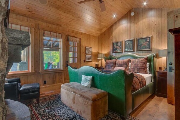 A wooden cabin bedroom with a bed, a green upholstered bench, a patterned rug, and a large window.