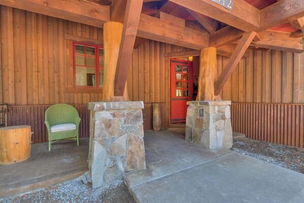 Una cabaña de madera con un porche de piedra, una silla verde y una puerta roja.