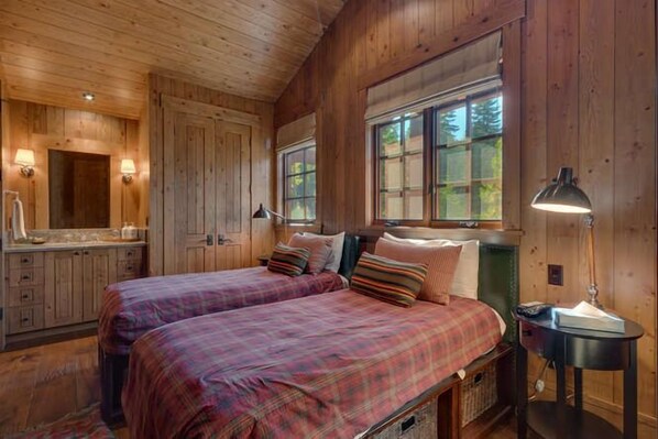 A wooden cabin bedroom with two beds, a nightstand, and a window.