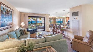 En rummelig stue med en stor sofa, et spiseområde med havudsigt og et køkken med moderne hårde hvidevarer.